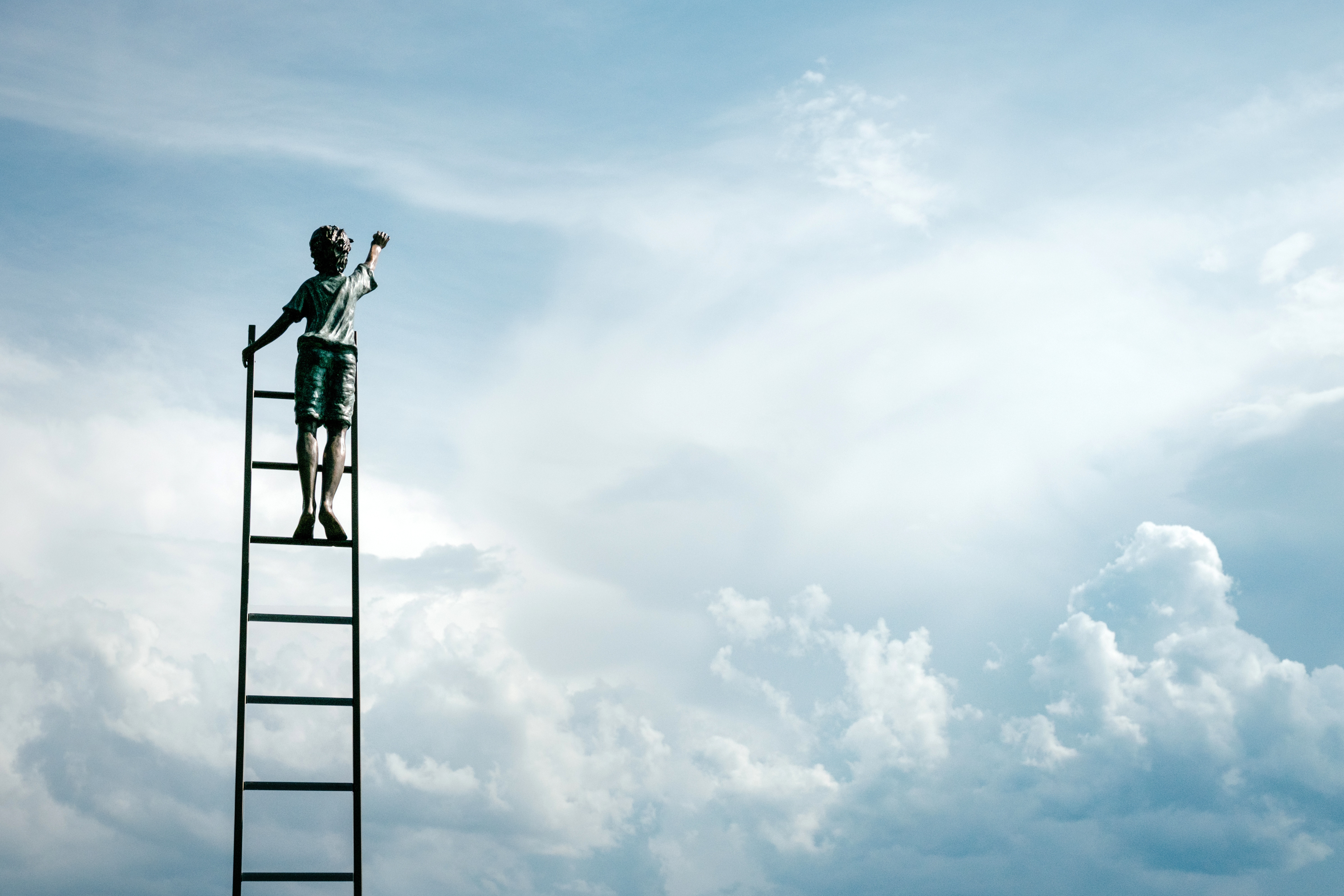 Boy on ladder reaching for clouds